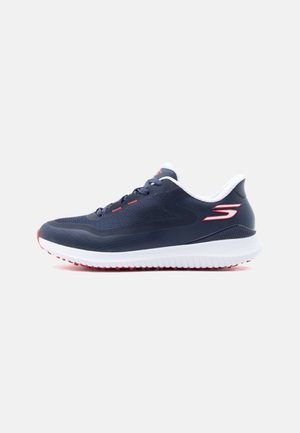 Scarpa da ginnastica atletica blu navy con suola bianca, particolari rossi, design con lacci e logo sul tallone su sfondo grigio chiaro uniforme.