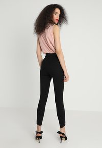 Svarte høydejusterbare skinnyjeans med detaljert søm og baklommer, kombinert med en lys rosa ermeløs topp. Svarte høyhælte sko.