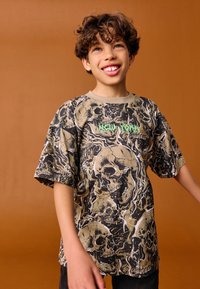 Tricou grafic cu model de craniu în negru, crem și verde. Tricoul are croială lejeră și este confecționat dintr-un material moale, cu mâneci scurte.