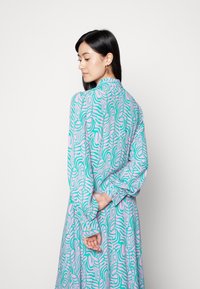 Vestido de manga longa com um padrão abstrato vibrante em turquesa e rosa, com um decote de colarinho e mangas bufantes enrugadas.