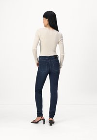 Csíkozott bézs hosszú ujjú felső fodros nyakkivágással, sötétkék, slim-fit farmernadrággal és fekete tömbsarokkal rendelkező szandállal párosítva. Minimalista dizájn.