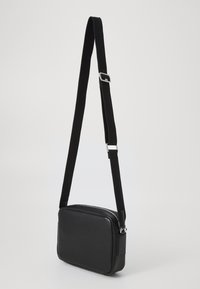 Borsa a tracolla sintetica nera con forma rettangolare, superficie testurizzata e una robusta tracolla regolabile con accessori in metallo argentato.