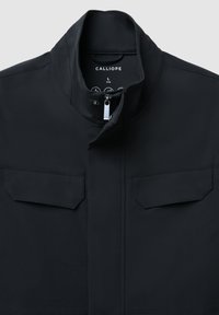 Giacca nera con colletto alto, chiusura con zip argentata e due tasche sul petto. Realizzata in tessuto liscio e resistente. L'etichetta riporta la scritta "CALLIOPE" in taglia L.