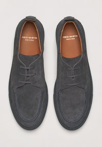 Chaussures en daim gris foncé à bout rond et à laçage minimal. Semelle en caoutchouc avec des accents beiges. Étiquette "Fred Martin" visible à l'intérieur.