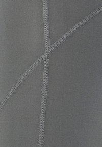 Šedá sportovní tkanina s hladkou strukturou. Obsahuje kontrastní ploché švy ve geometrickém vzoru. Žádné viditelné loga ani další detaily.