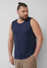 Donkerblauw mouwloos tanktop met een gladde textuur. Ronde halslijn en een subtiele merklogo op de borst. Combinatie met beige broeken.