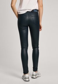 Černé skinny džíny z umělé kůže se hladkým povrchem, obsahující dvě zadní kapsy a středně vysoký pas, v kombinaci se stříbrnými sportovními botami.