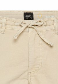 Beige Cordhosen mit elastischem Bund, seitlichen Taschen und einem schwarzen Etikett mit "camel active"-Branding. Strukturiertes Material.