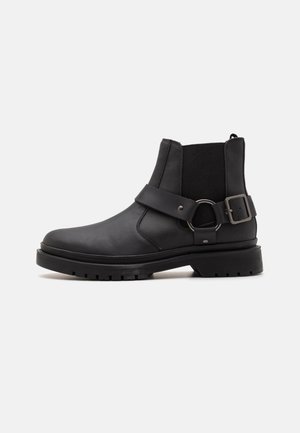 Botas de cuero negras hasta el tobillo con paneles laterales elásticos, un detalle de correa y hebilla, y una suela de goma texturizada para un mejor agarre.