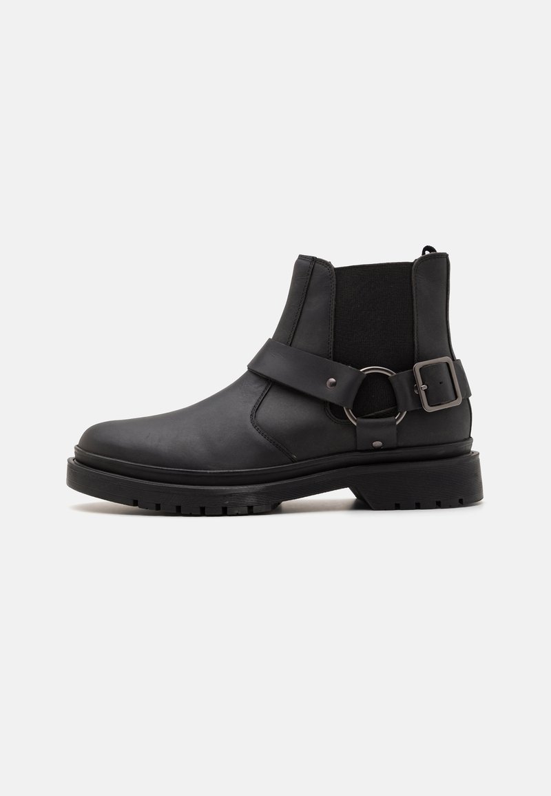 Botas de cuero negras hasta el tobillo con paneles laterales elásticos, un detalle de correa y hebilla, y una suela de goma texturizada para un mejor agarre.