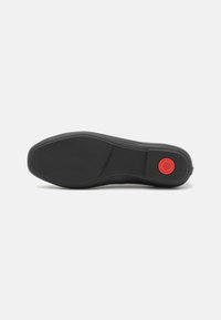 Semelle de chaussure en caoutchouc noir avec une texture lisse, une forme arrondie, des coutures visibles et un logo circulaire rouge près du talon.