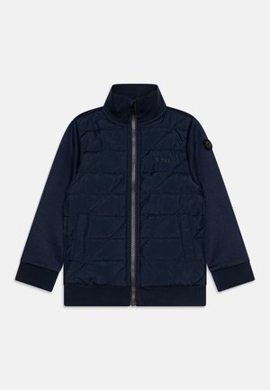 Veste bleu marine avec un devant matelassé, col haut, fermeture éclair sur toute la longueur et poignets côtelés ; présente un écusson logo sur la manche et des poches latérales.