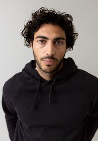 Sudadera negra con capucha y cordón, con una textura suave y mangas raglán, usada por una persona con cabello rizado.