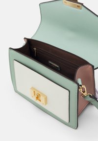 Bolso de mano de cuero verde y blanco con un broche dorado. El interior cuenta con un forro de tela marrón y un bolsillo con cremallera. Diseño estructurado con bordes suaves.