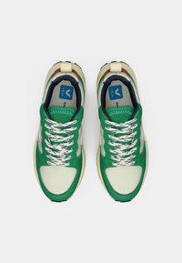 Rohelised ja kreemjad spordijalatsid tekstuurse kangaga, mustriliste paelte ja polsterdatud taldaga. Omavad sinist logo ja mitmevärvilisi aktsente.