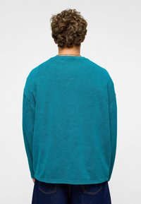 Teal trui met lange mouwen, losse pasvorm, gestructureerde stof, ronde halslijn, afgewerkte zoom en zichtbare stiksels langs de randen.