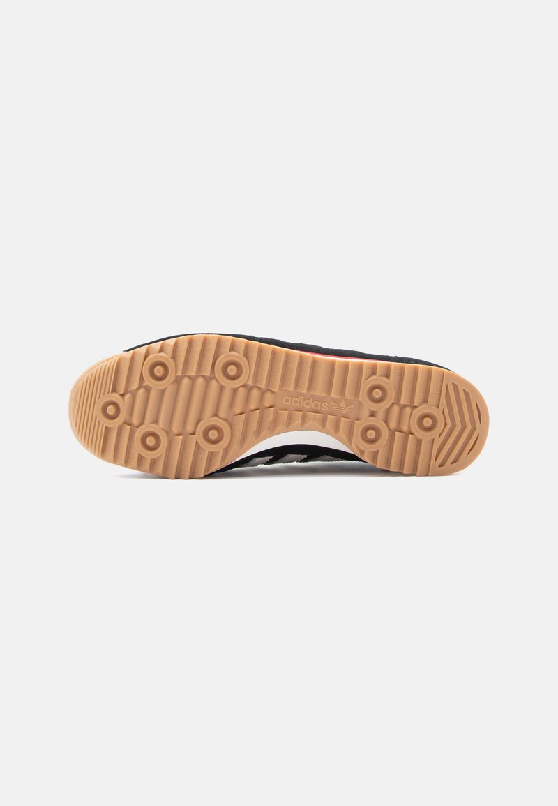 Adidas shoe sole with a textured, gum rubber base featuring circular studs and wave patterns, primarily black with white accents.