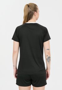 Svart sportt-shirt med korta ärmar och vit krage, slät textur, matchad med svarta shorts, bakvy visar blommighetatueringar på armen.