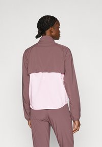 Πολυεπίπεδη ζακέτα με μοβ επάνω μέρος και ανοιχτό ροζ κάτω μέρος. Κατασκευασμένη από απαλό ύφασμα, με ψηλό γιακά και ελαστικό τελείωμα.