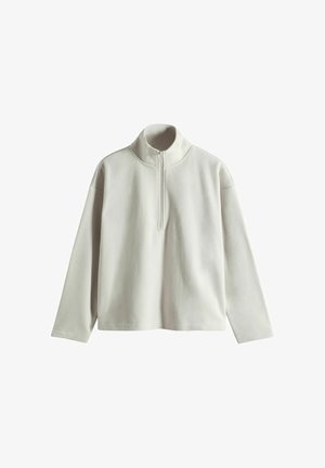 Suéter de manga larga en gris claro, con un alto cuello y media cremallera. El tejido parece suave, con una textura lisa y un ajuste ligeramente holgado.