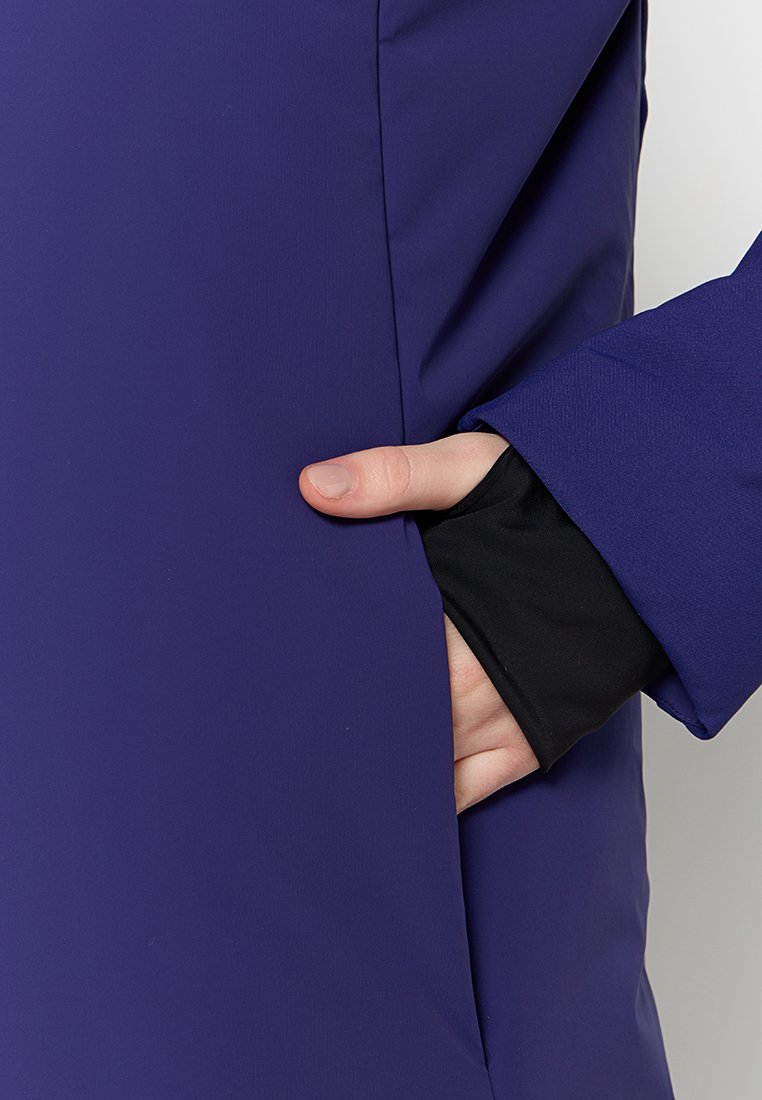 Dettaglio della tasca di una giacca impermeabile viola con un polsino interno nero. Texture liscia, design elegante, con una mano nella tasca laterale.