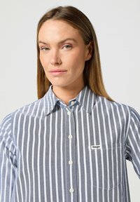 Skjorta med knäppning fram i grå och vita vertikala ränder, med krage, bröstficka och Wrangler-logga. Tillverkad i bomull, avslappnad design.