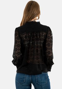 Blusa nera in pizzo con schiena arricciata, maniche lunghe e scollatura a onde. Il design presenta motivi geometrici su tutta la superficie.