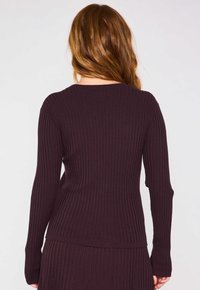 Maglione a coste di un viola scuro con maniche lunghe e scollo rotondo. La texture è finemente a coste, creando sottili linee lungo il tessuto.