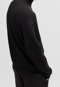 Pullover nero con collo alto, realizzato in tessuto morbido. Presenta una vestibilità comoda e orli a costine, con cuciture minimali per un aspetto pulito.