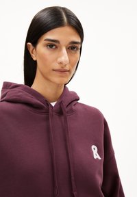 Bordeaux hoodie met een grote voorzak, trekkoord kap en wit lintlogo op de linkerborst; zachte katoenen stof.