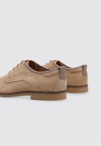 Zapatos de ante beige con un acento de tacón de cuero liso, punta redonda, diseño de cordones y una suela de goma minimalista.