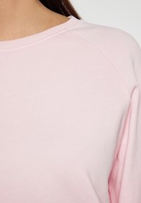 Lichtroze sweatshirt met een gladde stofstructuur, raglanmouwen en een ronde halslijn met subtiele stikdetails.