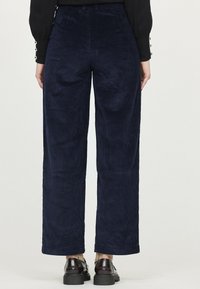 Pantalons larges en velours côtelé bleu marine avec une texture à côtes verticales. Dotés d'une taille haute et d'une coupe droite, avec des poches et une ceinture lisse.