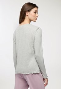 Camicia grigia chiaro a maniche lunghe realizzata in tessuto morbido, con scollatura rotonda e orlo scallop, abbinata a pantaloni rosa chiaro.