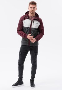 Färgblockerad jacka i burgundy, grå och svart. Har huva, dragkedja fram och sidofickor. Bärs med svarta cargobyxor och sneakers.