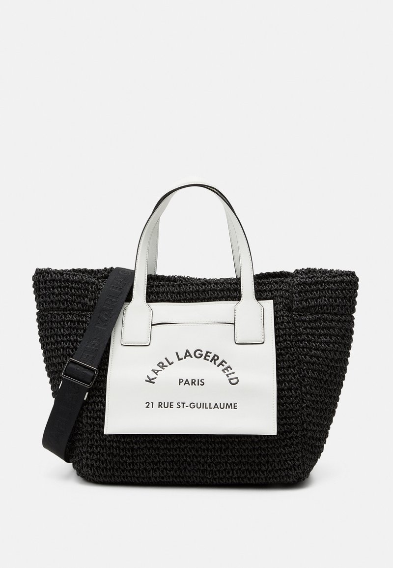 Svart vävd tote-väska med vita fusk läderdetaljer. Har en frontetikett med "Karl Lagerfeld, Paris" och avtagbar rem.