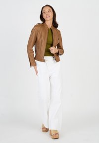 Bruine leren jas met een getailleerd ontwerp, ritszakken aan de zijkanten en schouderdetails; gecombineerd met een groene top en witte wijde broek.