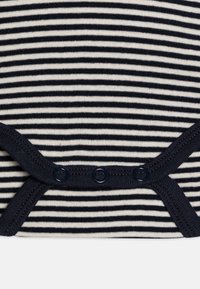 Body a righe blu navy e bianche realizzato in morbido cotone. Presenta chiusure a scatto nella parte inferiore e un colletto e aperture per le gambe a coste.