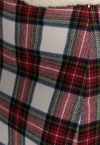 Tissu en tartan rouge, blanc et noir avec des accents verts. Tissage texturé avec des lignes verticales et horizontales formant des carrés. Image partielle d'un bord de vêtement.