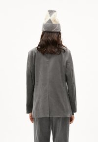 Grijze corduroy blazer met verticale strepen, voorzien van een enkele rugventilatie. Gecombineerd met bijpassende grijze broek en een gebreide muts met patroon.