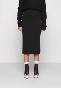 Svart stickad midikjol med hög midja. Kombineras med svartvita ankelstövlar med blommönster och fransiga vita strumpor.