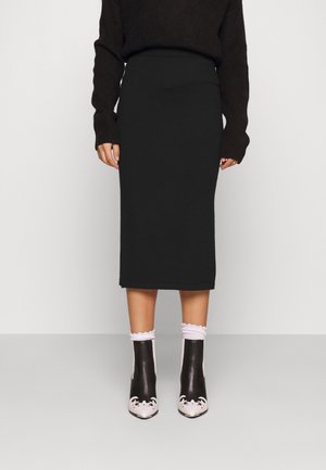 Jupe midi en tricot noir avec une taille haute. Associée à des bottines noir et blanc à motif floral et des chaussettes blanches bordées de volants.