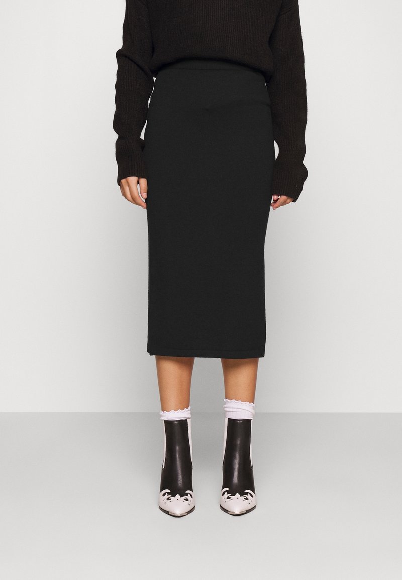 Svart stickad midikjol med hög midja. Kombineras med svartvita ankelstövlar med blommönster och fransiga vita strumpor.