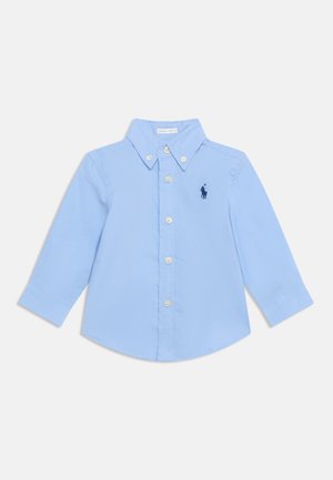 Lyseblå langærmet trøje til lille barn med knapkrave og knapper foran, med et lille mørkeblåt broderet logo på brystet.