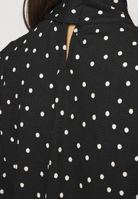 Tessuto nero con pois bianchi, dotato di una superficie testurizzata e un'apertura a chiave sul retro. Materiale morbido e leggero.