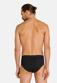 Schwarze Schwimm-Briefs mit glatter Textur, elastischem Bund und einem tief geschnittenen Beinausschnitt, von hinten vor einem weißen Hintergrund betrachtet.