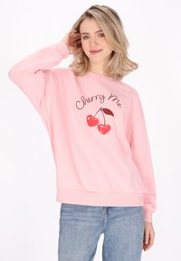 Felpa rosa con scollatura rotonda e spalle basse. Presenta una grafica di ciliegie e il testo "Cherry Me". Tessuto morbido e casual.