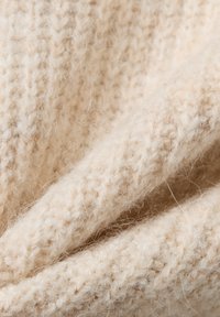 Beżowa dzianina o miękkiej, puszystej fakturze. Posiada tkany wzór z widocznymi włóknami, tworząc ciepły, przytulny wygląd.