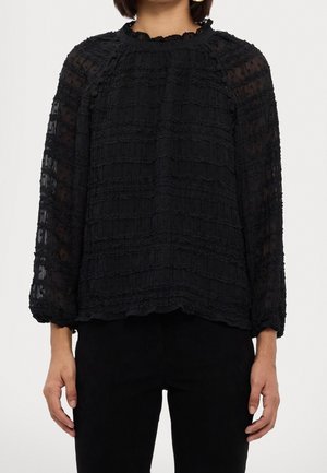 Black long-sleeve blouse with textured, ruffled fabric. High neckline with a gathered detail and loose fit. Paired with black pants.