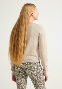 Beige knitted sweater with long sleeves, paired with animal print leggings featuring a gray and black leopard pattern. Long, wavy hair is styled down.